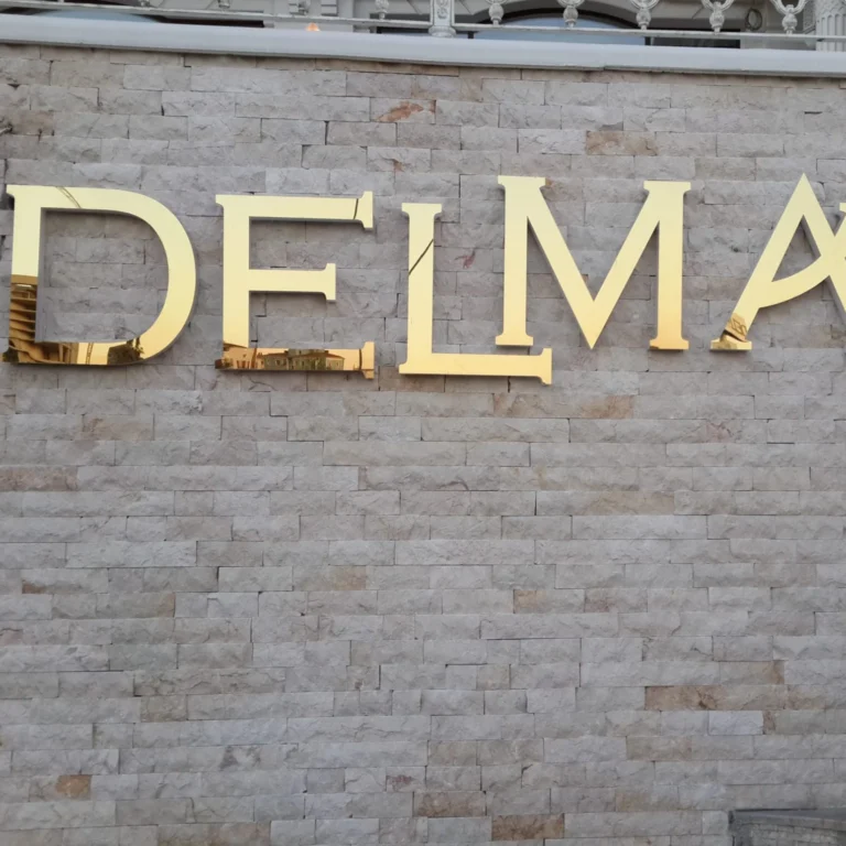 Taş duvara monte edilmiş parlak altın renkli paslanmaz kutu harf tabela
